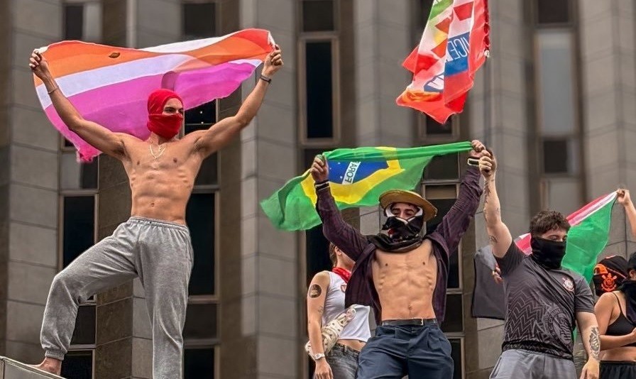 Manifestantes sem camisa e mascarados erguem bandeiras em cima de estrutura na Avenida Paulista durante ato pró-Lula